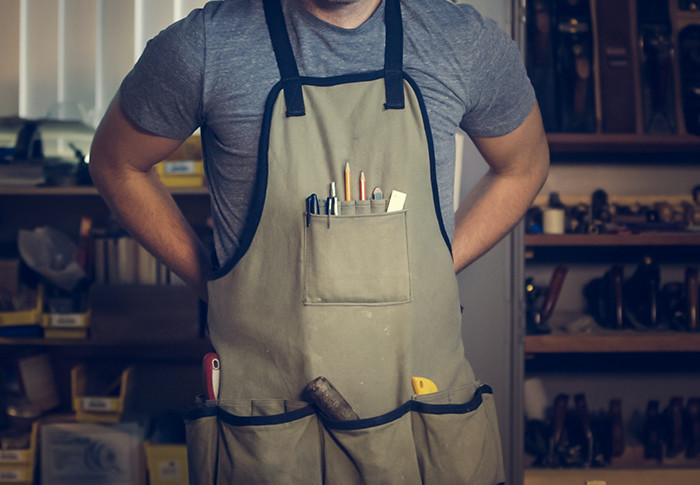 Tradesman tying the strap of an apron with tools in its pockets.